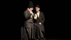 two clowns in black sitting on a suitcase