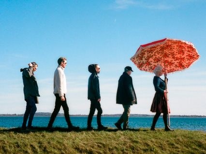 fem mennesker går ved vandet med en parasol - Evy Konigsberg