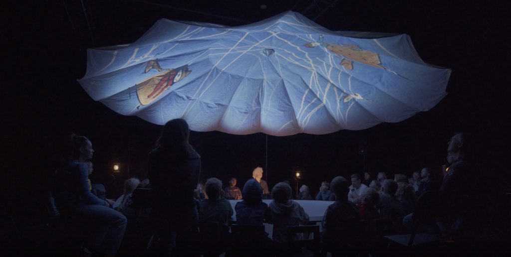 foto fra forestillingen Det hemmelige bibliotek, hvor du ser et loft, der ligner en teltdug, fyldt med projekterede billeder med publikum siddende under