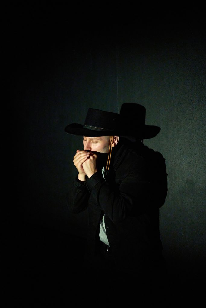 mand med sort hat med skygge på dækker det nederste af sit ansigt og skuler til kamera