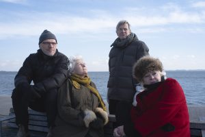 to mænd og to kvinder sidder ude med vandudsigt bag dem