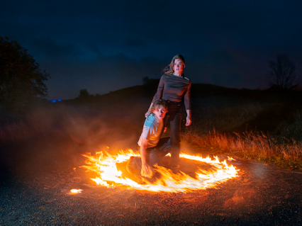 ung mand og ung kvinde inde i ring af ild på en strand i mørke - pressefoto fra forestillingen Hydra krisen venter med teatergrad på teatrte grupep 38