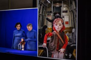 jeg ser dig_dukkedreng i tog samt mand og kvinde klædt i blå med dkker ihænderne